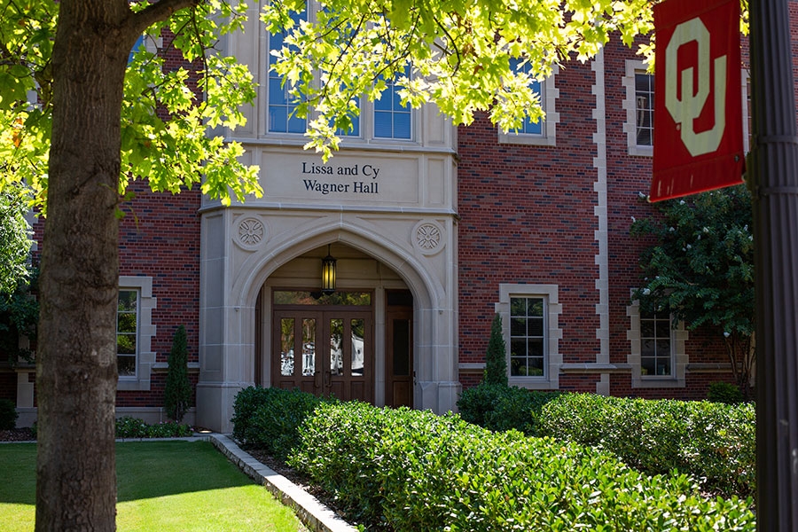 The entrance to Lissa and Cy Wagner Hall, with greenery and an OU flag in the foregound.