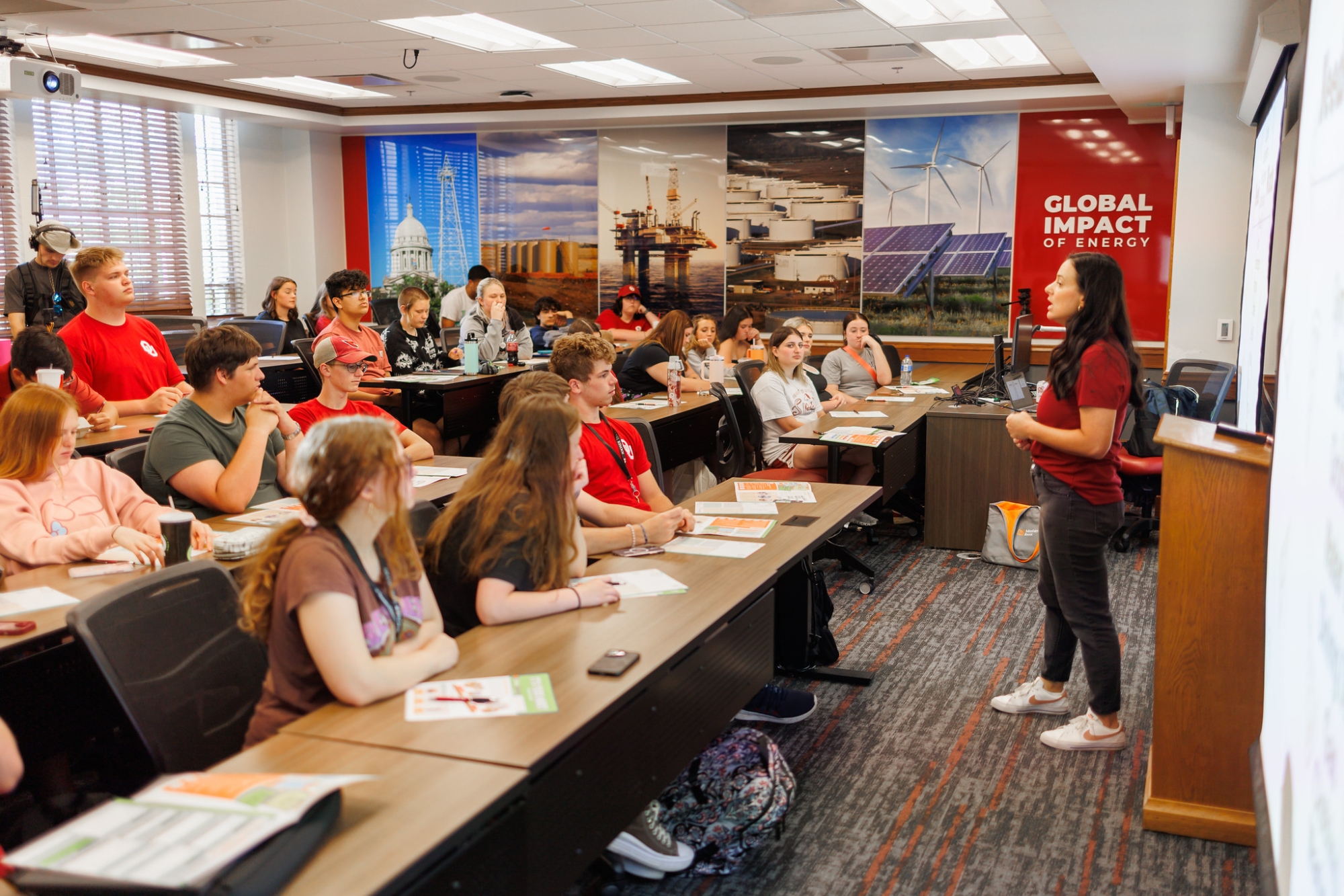 Instructor speaking with group of students sitting at classroom tables