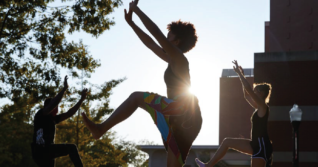 A group of people practicing yoga poses while backlight by the sun.