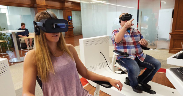 Two students with VR headsets sitting in a glass-enclosed room.