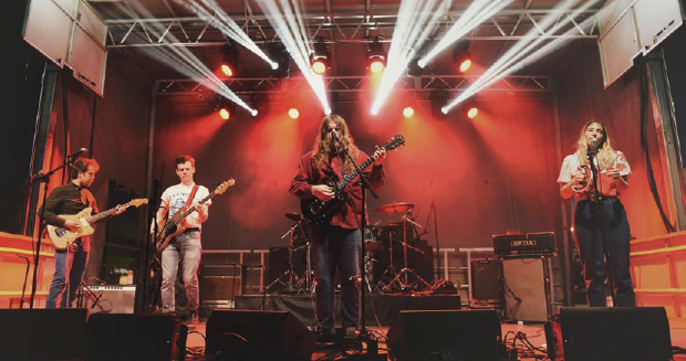 Musicians perform on a stage backlit with red and white lights.