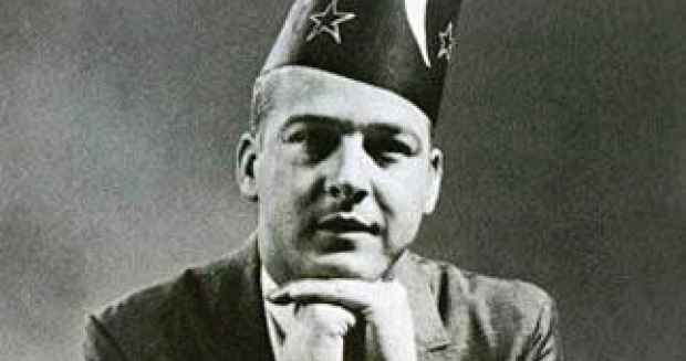 A black and white photograph of a man wearing a cone-shaped hat.
