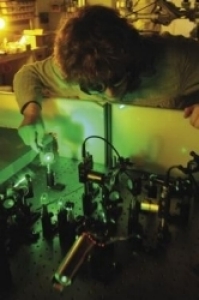 A graduate student wears protective eye glasses while working on an optical lab bench setup.