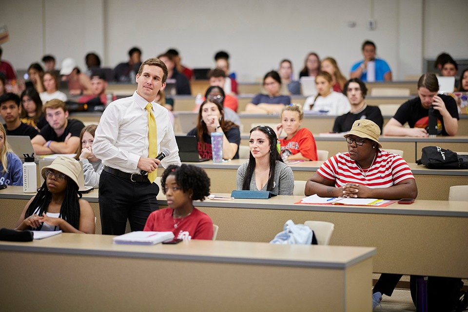 Political Science GTA standing and holding microphone with students in a classroom.