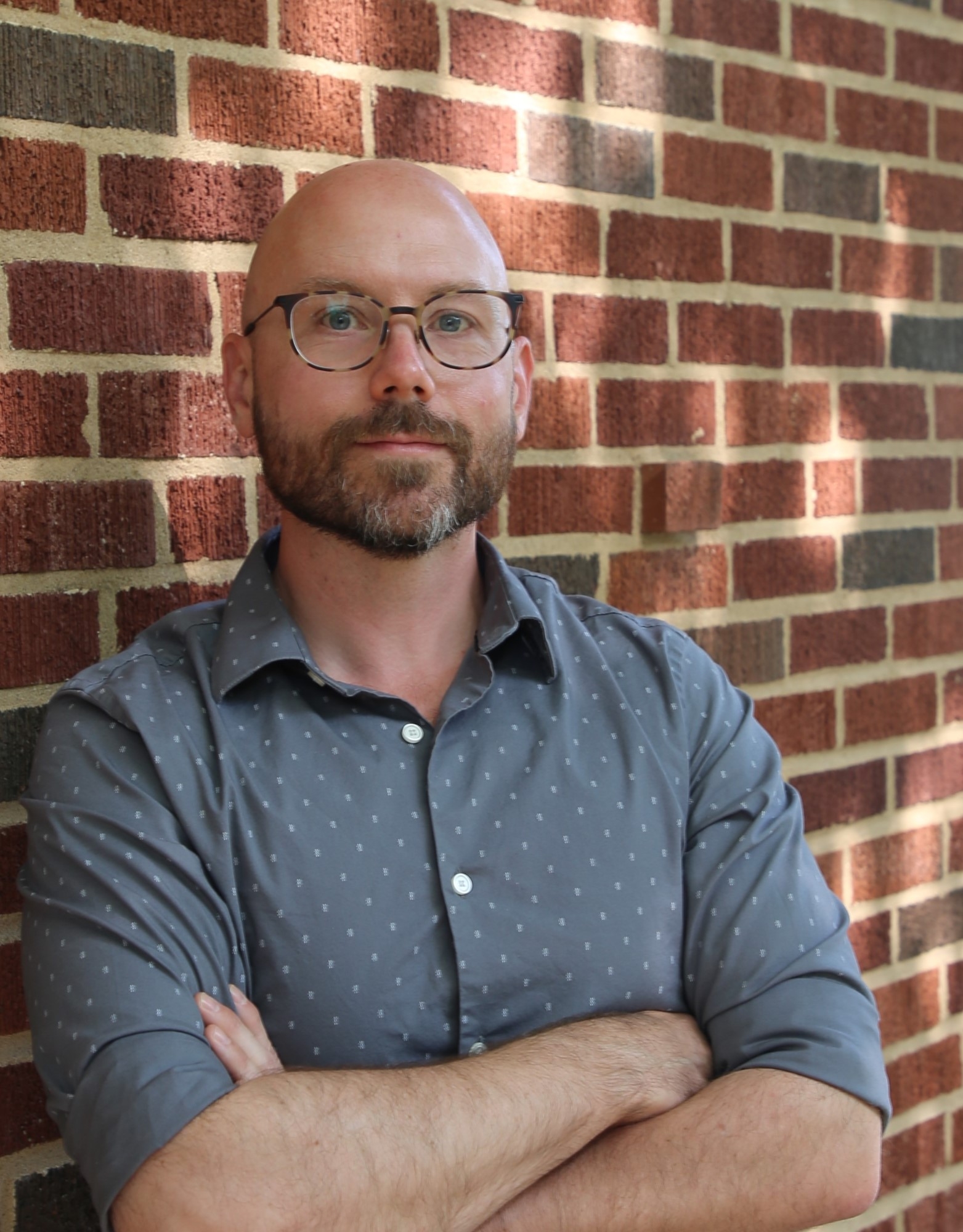 David Allen, gray shirt, arms crossed, with a brick wall behind him
