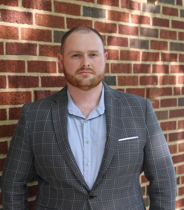 William Hanby III, in a gray blazer, with a brick wall behind him.