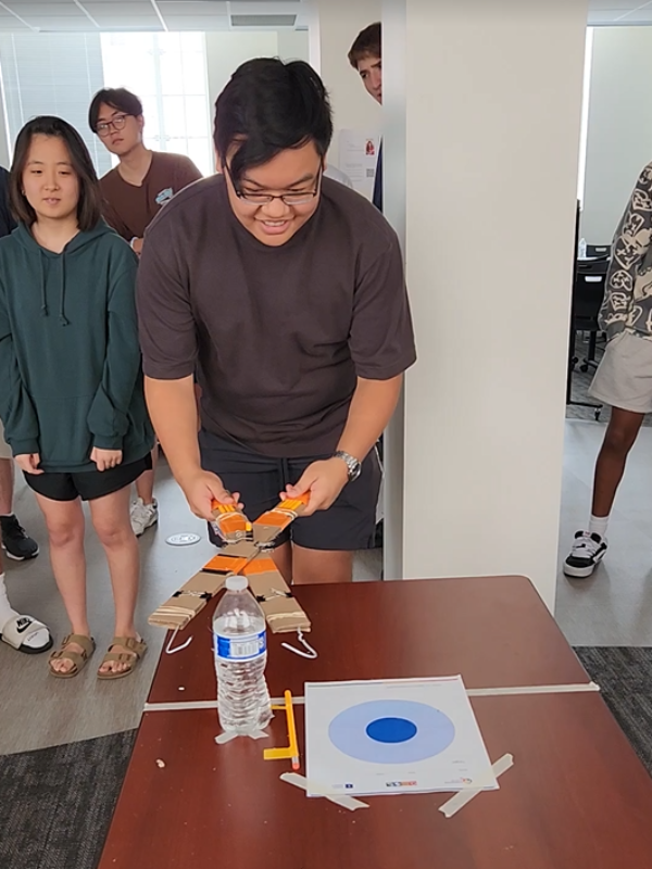 Student using a robot arm constructed in class to pick up a water bottle