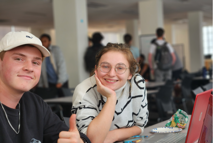 Two students sitting next to a computer, smiling. One is giving a thumbs up