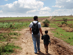 Man with boy walking down dirt road with small boy in Africa.