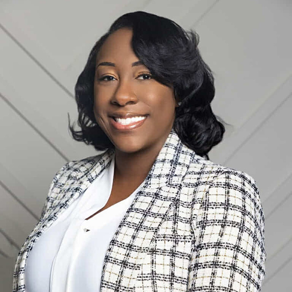 Woman with long dark/carmel hair wearing a white blouse and black and white blazer.