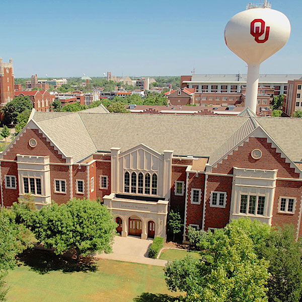 Historic brick building on the Norman campus. A water tower with O U is visible in the distance.