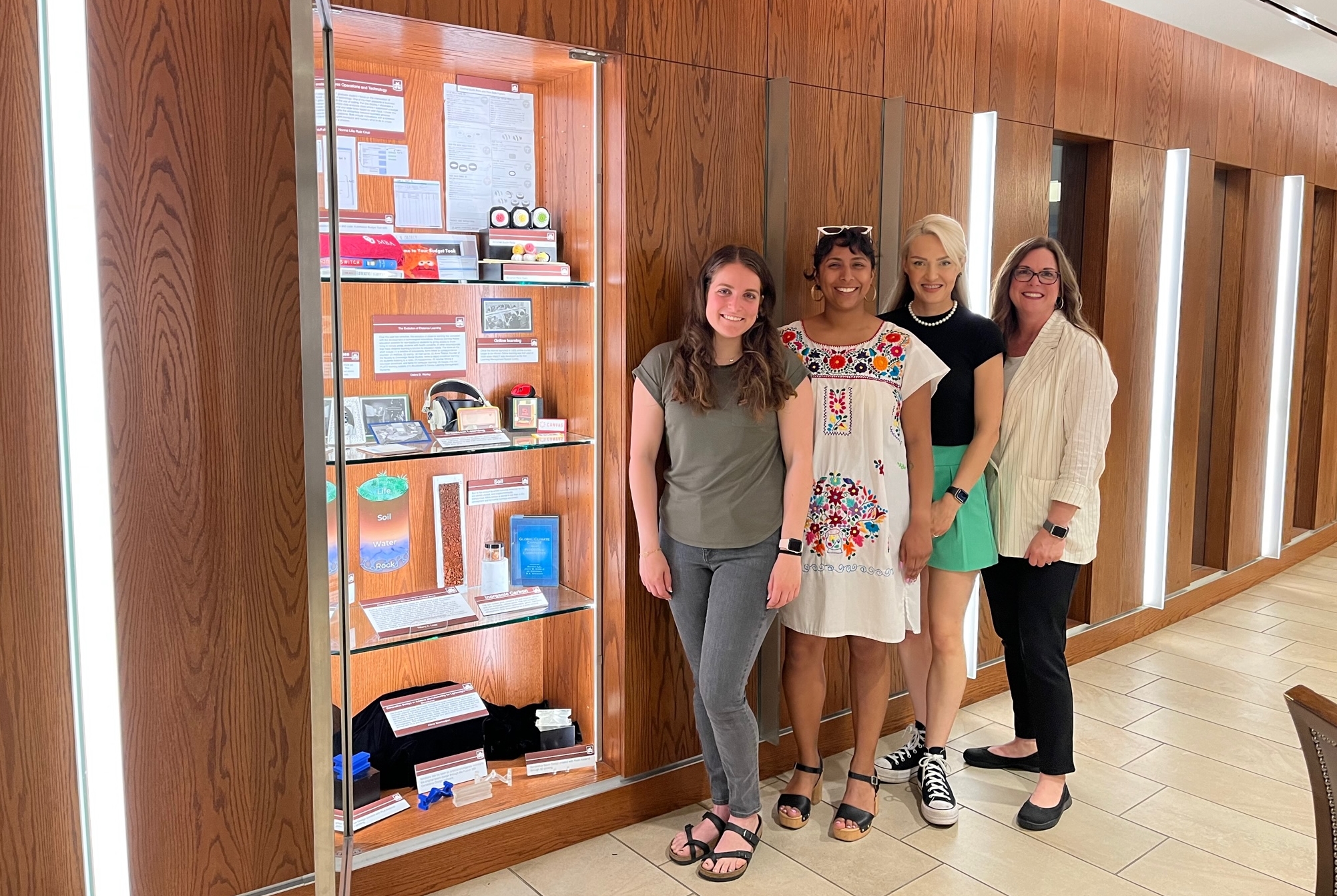 Four individuals standing next to a display of historical and research items on a glass shelf.
