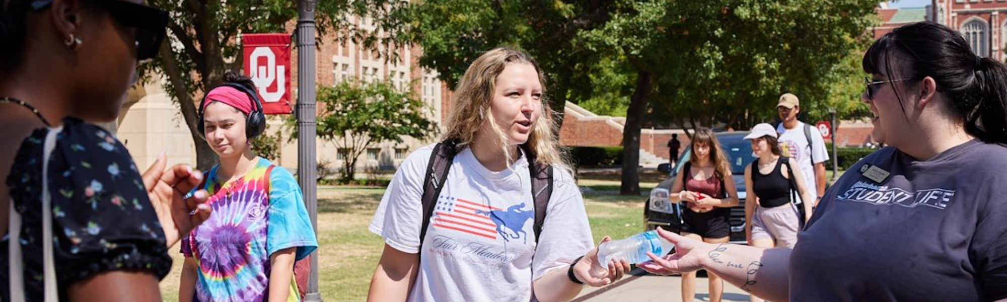A 学生生活 staff member handing a student a bottle of water.