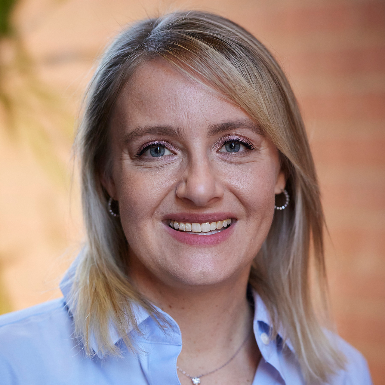 woman in a blue oxford shirt with blonde hair smiling