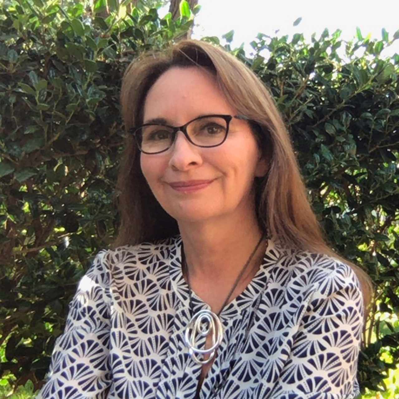 Woman with long brown hair and glasses wearing a black and white print top