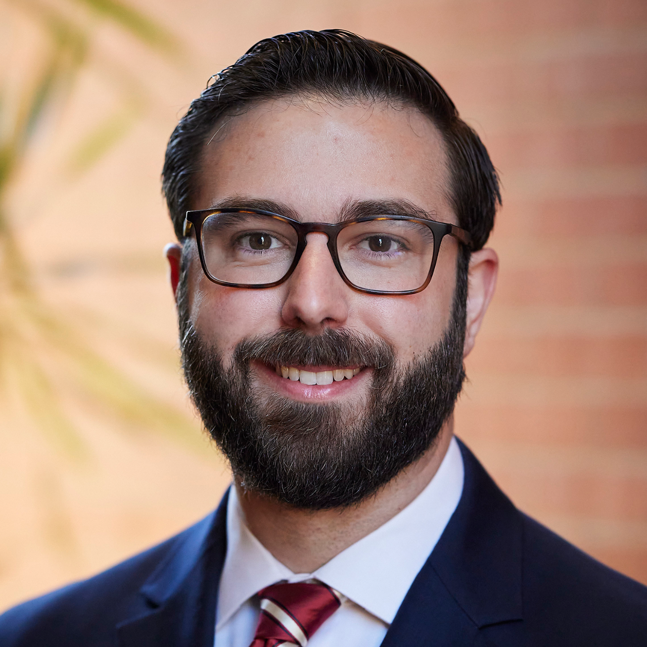 Man in white shirt with navy blazer, glasses, dark hair and a dark beard