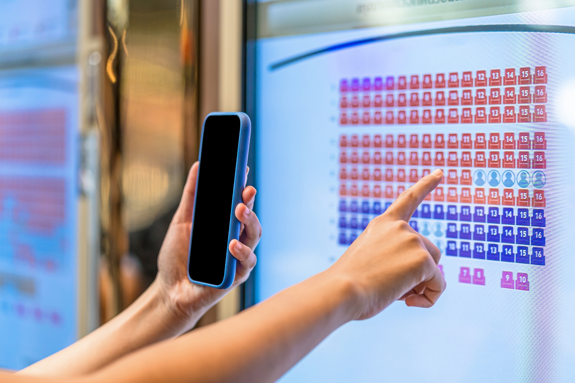 Person holding a cell phone in the their left hand, pointing at a screen with numbers.
