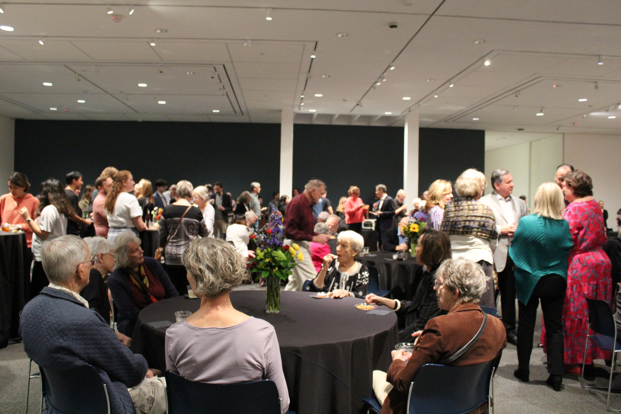 Large group event standing and sitting at tables in gallery space. 