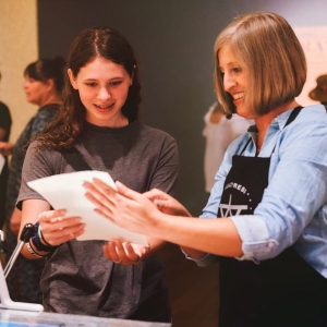 Educator showing teenager how to print with a printing press. 