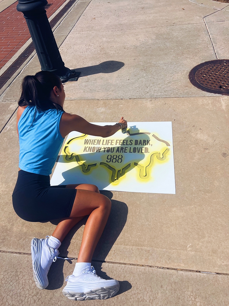 Students paint the sidewalk with an advertisement for 988.