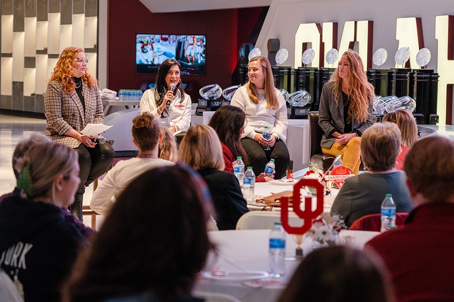 A panel setup where four women are seen looking at each other while one is talking to the crowd