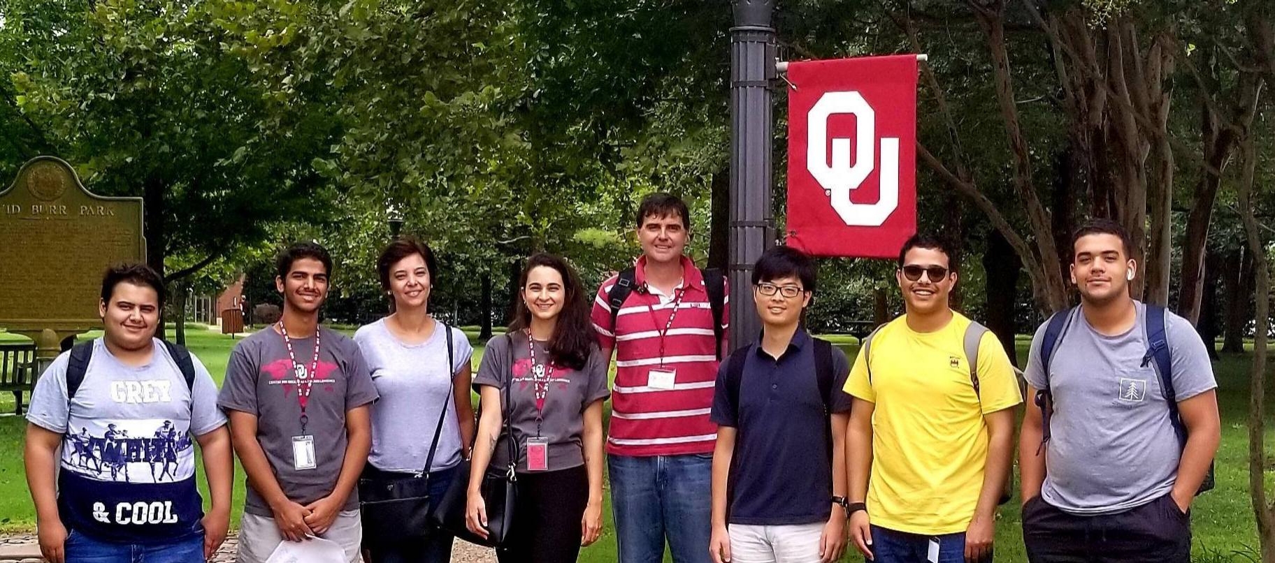 group of seven people standing in a line outdoors near OU flag