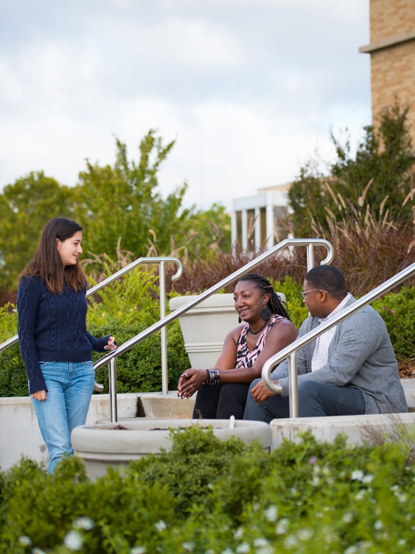 Three students sitting and standing on stairs, talking.