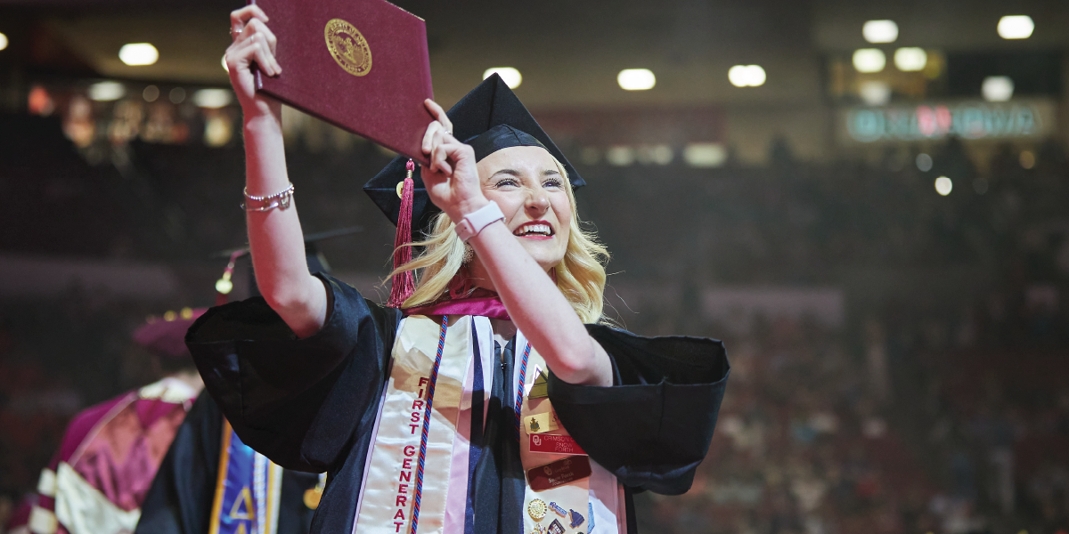 First-Generation Graduate Female First-Generation graduate in cap and gown holding a diploma cover at OU's commencement ceremony.