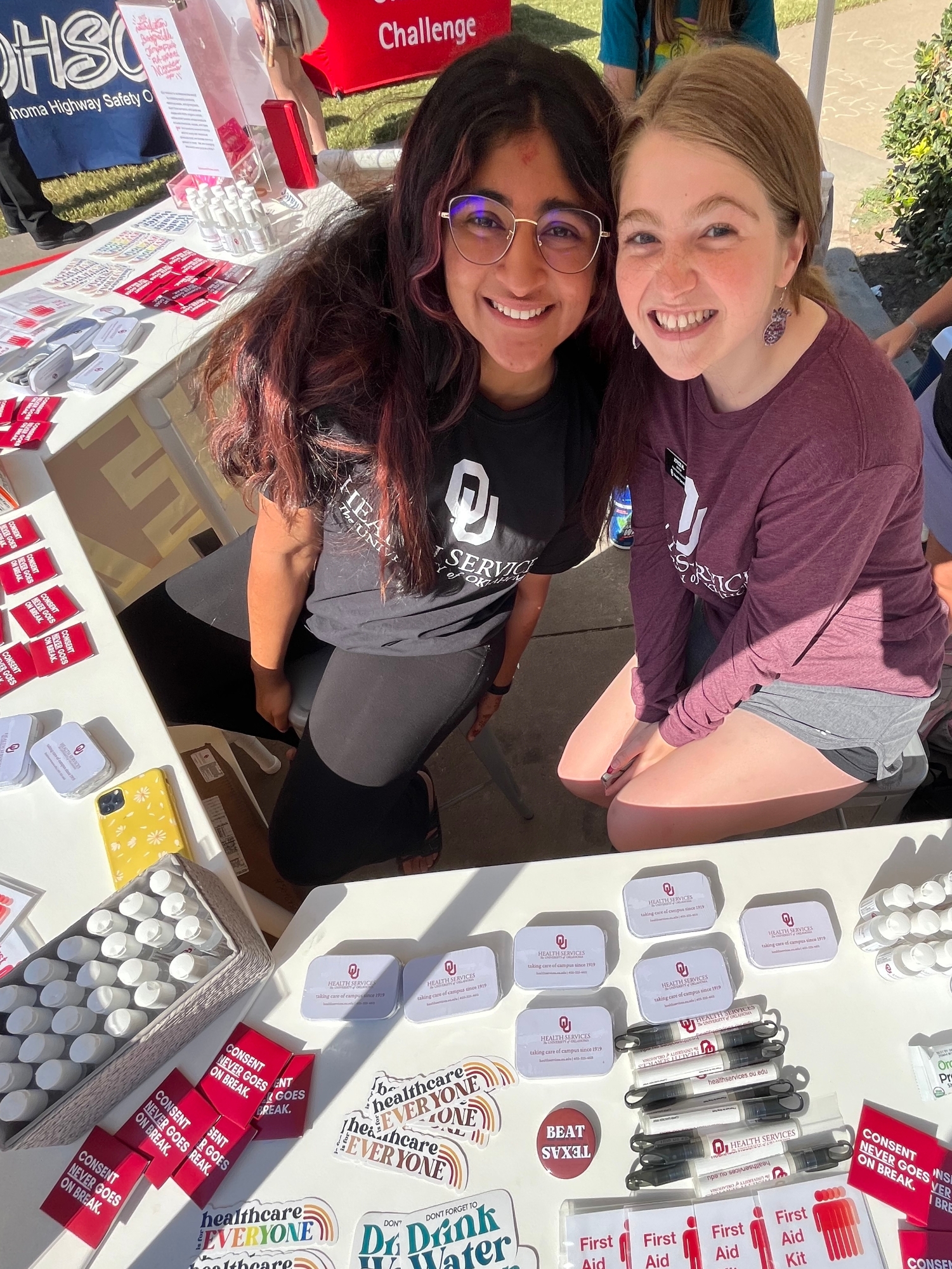two students smiling at health hut while giving away hand sanitizer