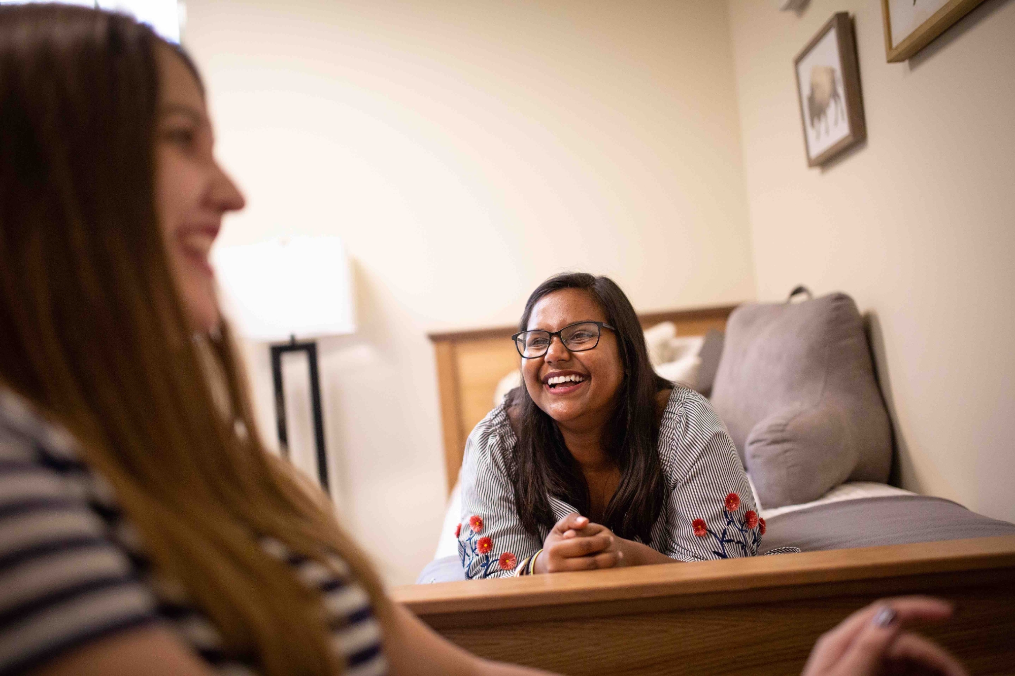 Two female roommates talking to one another in their room in the Residential Colleges. One is lying in her bed while the other is sitting at a desk.