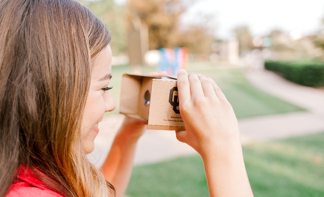 Person holding virtual reality glasses on campus.