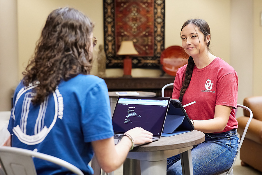Two students sitting at a table with laptops.