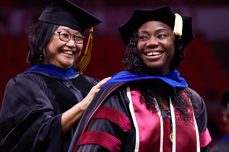 An OU doctoral graduate is hooded by a faculty member.