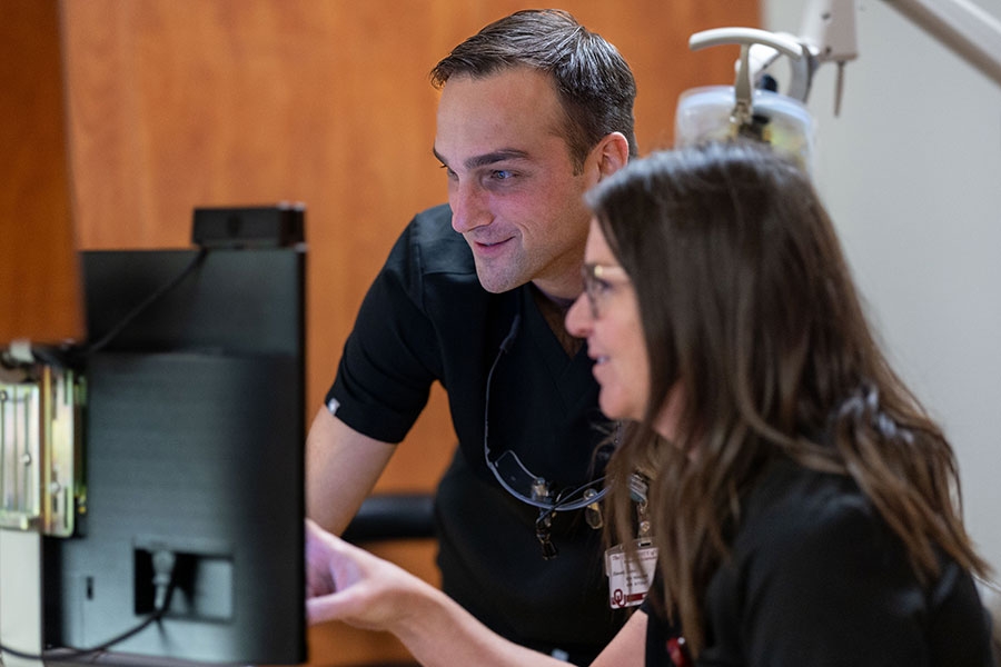 Two people in black scrubs look at a computer screen.