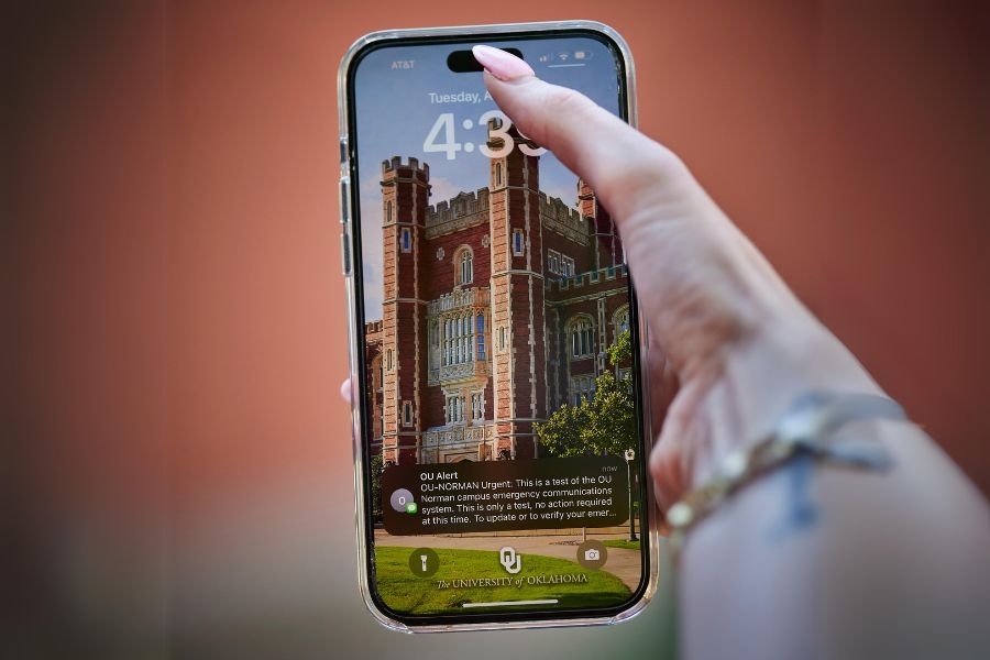 A hand holding a phone showing an OU-Alert text.