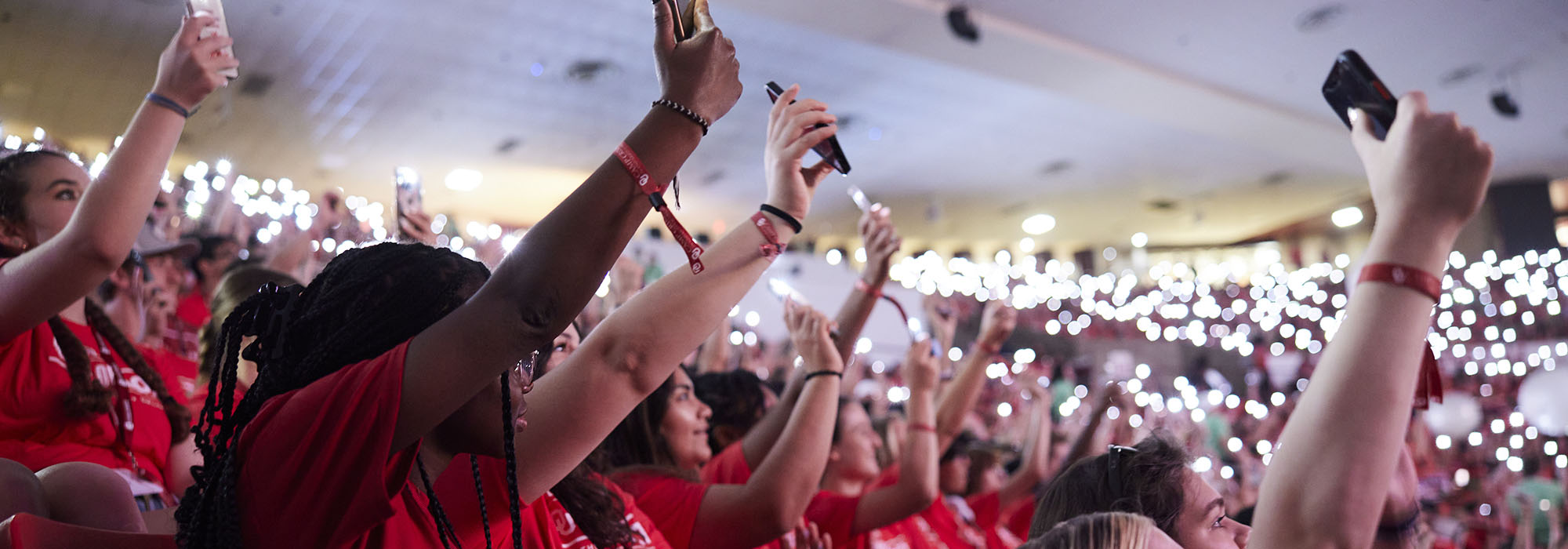 Campers in the stands holding up phone flashlights during 营深红色 opening session.