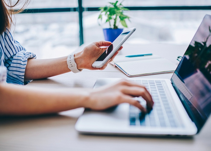 A person sitting at a table with their phone and laptop.