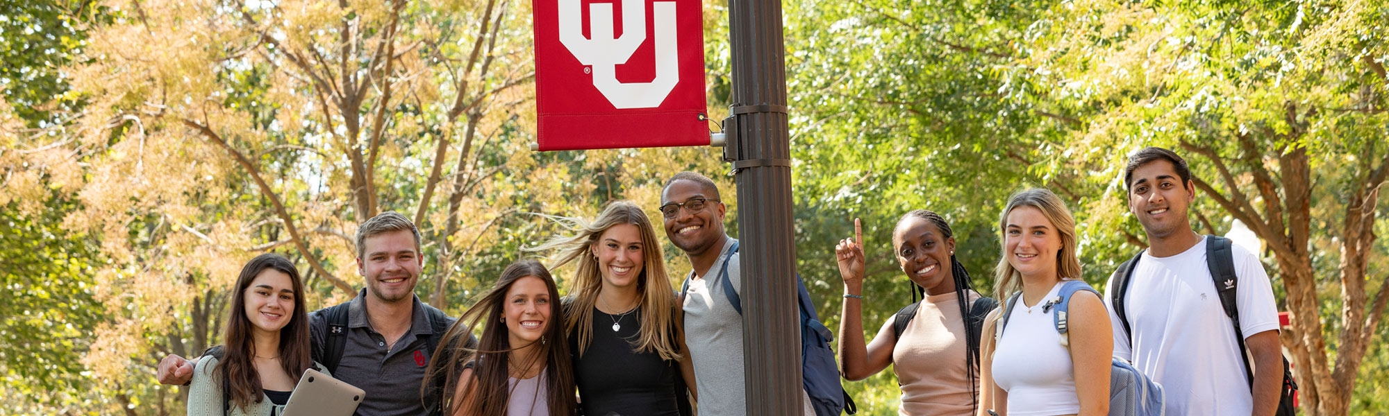 A group of OU students on campus standing together near a lamppost decorated with anOU flag.