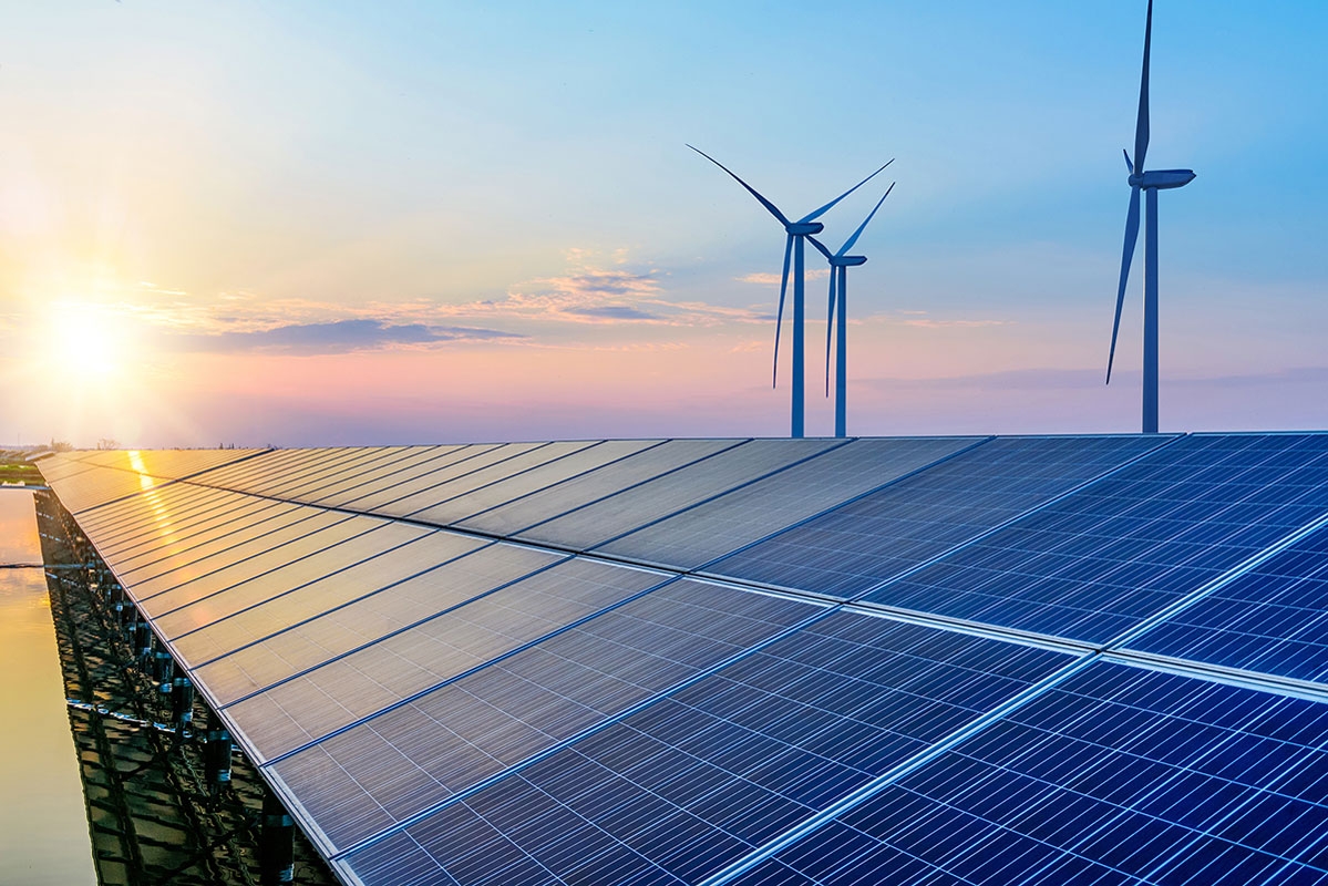 Solar panels and a wind turbine against a setting sun. 