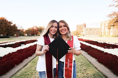 Elizabeth and Sarah Cermak pose together holding a graduation cap on OU's South Oval