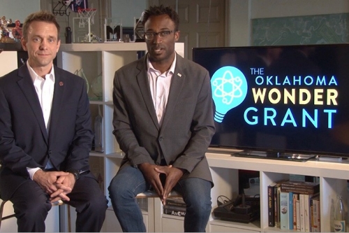 representatives from Oklahoma Wonder Grant sit in front of a display screen that displays the Oklahoma Wonder Grant logo