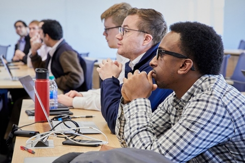 Several students sit at a table in class listening intently