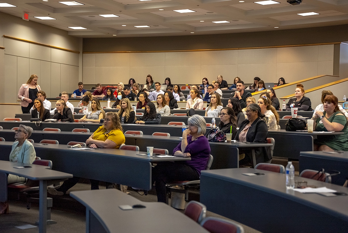 Students sit in a large, audotorium style room listening to a presenter