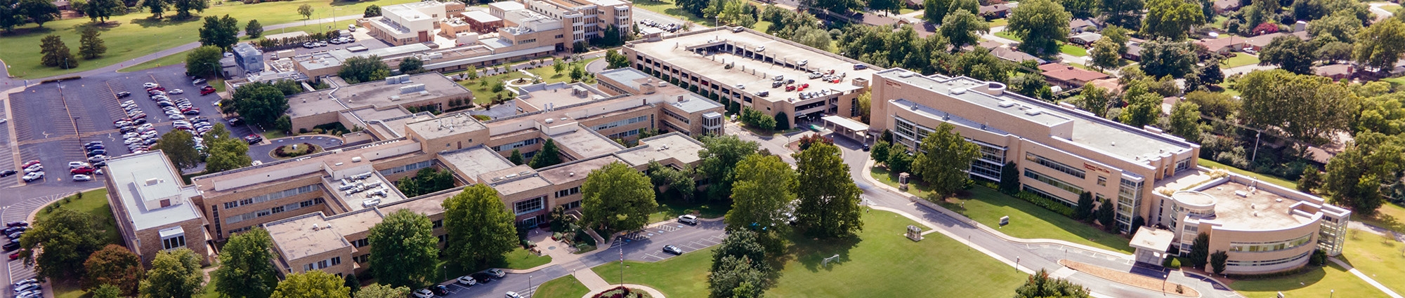The modern OU-Tulsa campus is show in an aeral view, green hills and trees stretching into the distance