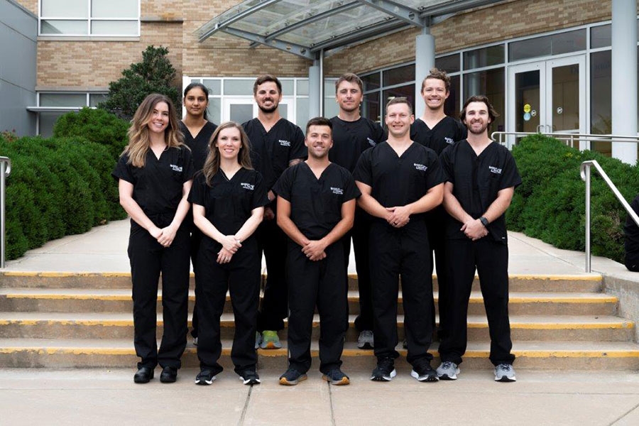 The class of 2027 students in black scrubs, standing on stairs.