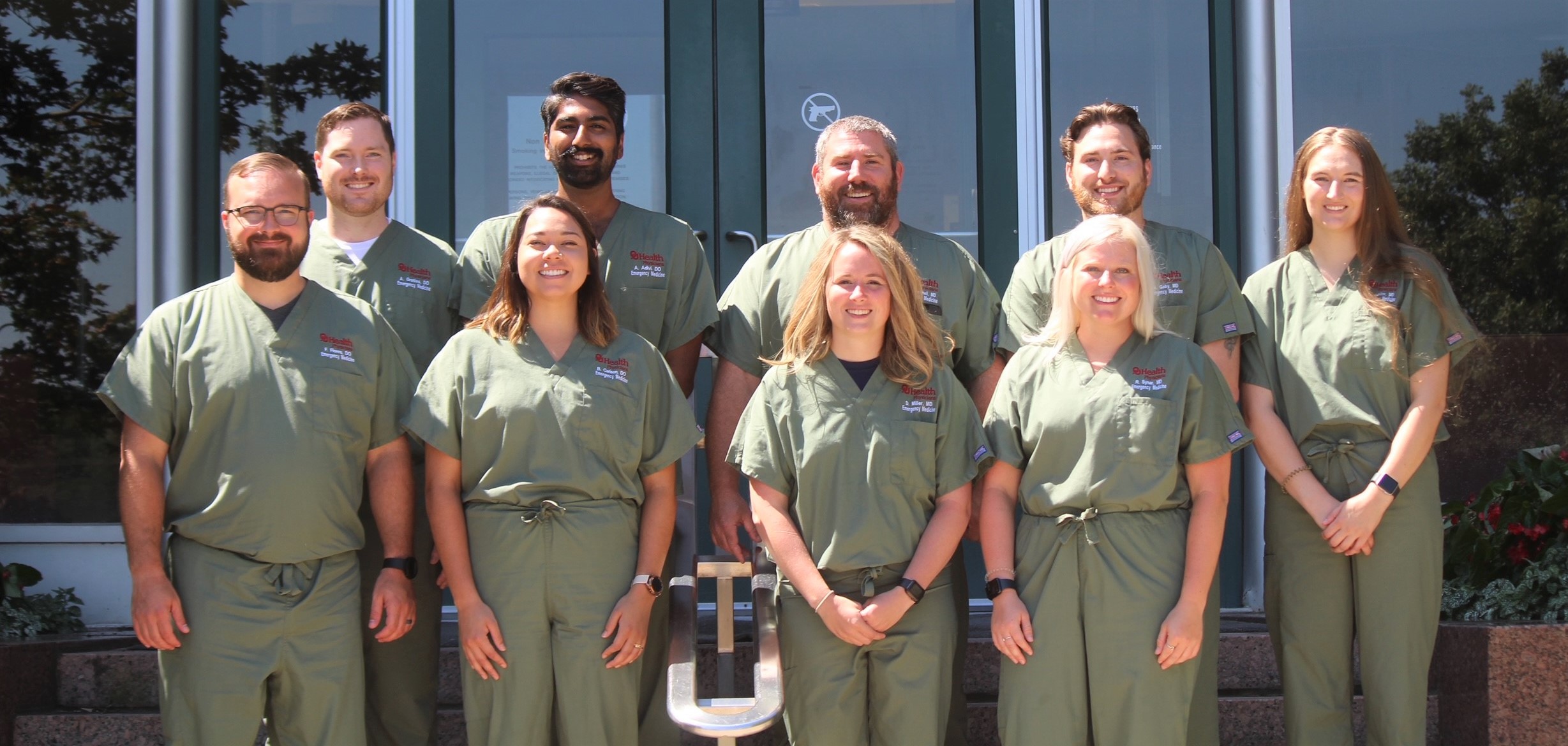 Nine individuals wearing green scrubs, posing for a group photo.